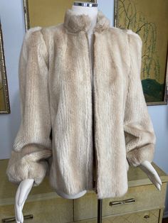 "What a beautiful way to keep the chill away! The faux fur coat is so soft and cozy. It is lined in apricot colored satin. It zips closed at the front and buttons at the throat. The sizing is most comparable to a modern size medium, but please go by the measurements to ensure a fabulous fit. I could find no issues. In wonderful condition, this beauty will keep you warm and stylish! Measurements taken with the item laid flat. Please compare them to a similar item in your own closet. Shoulders: 14 Beige Faux Fur Coat For Fall, Cozy Spring Fur Coat With Faux Fur Lining, Spring Cozy Fur Coat With Faux Fur Lining, Vintage Cream Fur Coat With Faux Fur Trim, Cream Fur Coat With Faux Fur Trim For Fall, Cream Faux Fur Trim Coat For Fall, Beige Fur Coat With Faux Fur Trim For Spring, Cozy Beige Fur Coat For Cold Weather, Beige Faux Fur Coat For Cold Weather