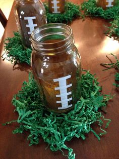 three mason jars with football painted on them sitting on top of green grass covered ground