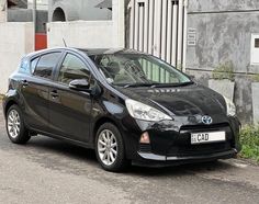 a small black car parked on the side of the road next to a building and grass