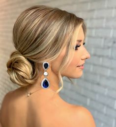 a woman with blonde hair in a low bun and pearls earrings on her head, looking off to the side