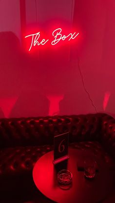 a red neon sign that reads the box above a table in a dimly lit room