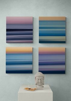 three abstract paintings hang on the wall above a white table with a buddha statue in front of it