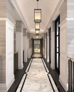 a long hallway with white walls and black trim on the floor is flanked by tall columns