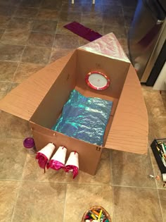 an open cardboard box on the floor next to some crayons and other items