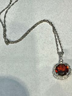 14K White Gold Diamond & Garnet scalloped Halo fancy pendant. This Halo pendant features a beautiful faceted 2.18ct round 8mm red Garnet stone, surrounded by diamonds, 0.05ctw. the chain is a 14K white gold rope chain, 1mm, 18" longThe arrangement of its facets is similar to that of a round brilliant, designed to maximize light and color. The sides are fancy scroll work with an open back. The stone is set in a 14K white gold prong setting which has an attractive halo design and holds the garnet Elegant Garnet Jewelry With Diamond Accents, Red Round Necklace With Brilliant Cut, Red Jewelry With Brilliant Cut Round Stone, Red Round Necklaces With Brilliant Cut, Red Pendant Necklace With Diamond Accents, Elegant Garnet Jewelry With Brilliant Cut, Red Garnet Jewelry With Diamond Accents, Fine Jewelry: Brilliant Cut Garnet, Fine Jewelry With Brilliant Cut Garnet