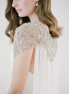 the back of a woman's white dress with beading on her shoulders and shoulder