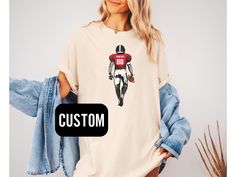 This football shirt is a great gift for any football fan that wants to show off their favorite player..  ✨Shipping & Processing - Please allow 2-5 business days for your item to be processed and printed. Processing times may be longer during busy holiday periods. - Your order ships from the US. Allow 2-7 business days shipping. Unfortunately, I am unable to guarantee USPS shipping times. ✨Returns✨ If there is a defect with your order, please reach out to us within 15 days of receiving the item. Customizable T-shirt For Football Season, College Football Season Short Sleeve T-shirt, Varsity Football Season Fan Gear T-shirt, Varsity T-shirt For Football Season Sports Events, Varsity Style T-shirt For Football Season Fan Gear, Varsity Style T-shirt For Football Season, Sporty T-shirt For Game Day During Football Season, Sporty T-shirt For Game Day Football Season, Sporty T-shirt For Football Season Game Day