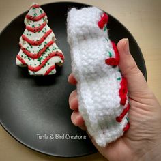 a hand holding a piece of crochet next to a small christmas tree on a black plate