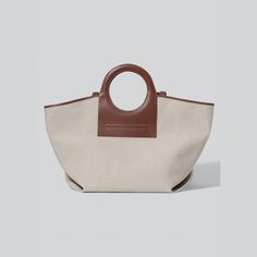 HEREU tote bag in canvas with leather trim. Ring top handles. Fabric lining. 15"H x 26"W x 9.8"D. "Cala" is made in Spain. Modern Large Capacity Canvas Bag With Double Handle, Modern Canvas Bag With Large Capacity And Top Handle, Modern Canvas Bag With Top Carry Handle, Beige Tote Weekender Bag With Handles, Top Handle Weekender Bag For Shopping, Shopping Weekender Bag With Detachable Handle, Canvas Bag With Handles For Errands, Beige Weekender Bag With Top Carry Handle, Modern Brown Coated Canvas Bag