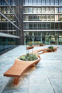 two wooden benches sitting next to each other on top of a stone floor in front of tall buildings