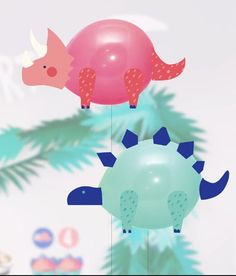 two dinosaur mobiles hanging from strings on a tree branch, one pink and the other green