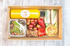 a box filled with fruits and vegetables on top of a white wooden table next to an orange juice bottle