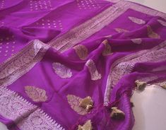 A Handwoven Purple Banarasi Georgette Kadhuwa Saree to make you stand out in a crowd. Furthermore, the saree is weaved all over with golden & silver zari in a beautiful kadhuwa weave pattern. Thus, this saree is for those who love handloom and have a taste for traditional attire. Also, it comes with blouse piece. Note: Banarasi Khaddi Georgete is a very soft and drapy fabric. Additional Information Color : Purple Zari Color: Golden and Silver Technique: Banarasi Kadhuwa Weaving Fabric: Pure Khad Celebration Tussar Silk Dupatta With Gota Work, Silver Handloom Dupatta For Festive Occasions, Silver Silk Dupatta For Festivals, Banarasi Silk Dupatta With Gota Work For Celebration, Silver Handloom Dupatta For Festivals, Tussar Silk Saree With Gota Work For Celebrations, Elegant Katan Silk Saree With Gota Work, Festival Celebration Saree With Zari Weaving, Traditional Silver Dupatta With Gota Work