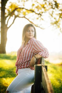 a woman leaning on a rail in the grass with trees in the backgroud