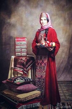 a woman in red is standing next to a pile of pillows and rugs, holding a tray