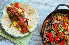 two tacos with meat, peppers and onions are on the table next to each other