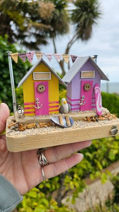 a hand holding a miniature house made out of wooden planks with beach scenes on it