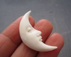 a hand holding a tiny white moon with a face carved into it's side