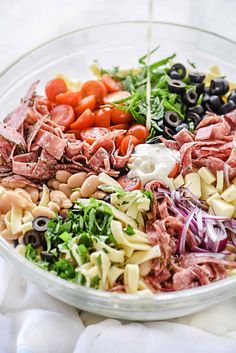 a salad with meat, olives, lettuce and tomatoes in a glass bowl