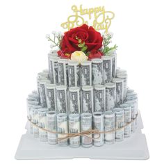 a cake made out of stacks of money with a red rose on top and happy new year written in gold