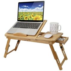 a laptop computer sitting on top of a wooden table next to a coffee cup and mug