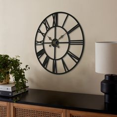 a large clock on the wall next to a table with a potted plant and lamp