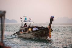 two people in a boat on the water with flags flying from it's masts