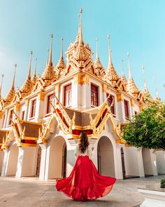 a woman in a red dress is walking towards a building with gold trimmings