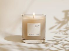 a candle with a label on it sitting in front of a white wall and shadow