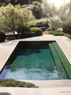 an outdoor swimming pool surrounded by shrubbery and trees in a garden area with water running through it