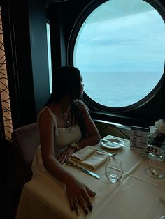 a woman sitting at a table in front of a large round window looking out on the ocean