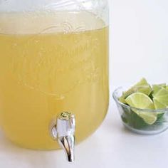 a glass jar filled with lemonade next to a bowl of limes