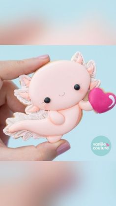 a hand holding a small pink toy with angel wings and a heart on it's finger