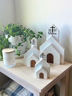 three small white houses sitting on top of a table next to a potted plant