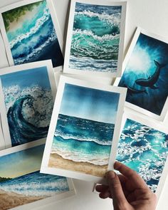 someone is holding up some watercolor paintings in their hand while they are showing them how to paint waves