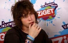 a young man with long hair wearing a black shirt and bracelets on his wrist