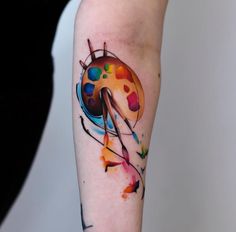 a ladybug tattoo on the arm with paint splatters