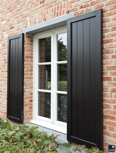 an open window with black shutters on a brick building