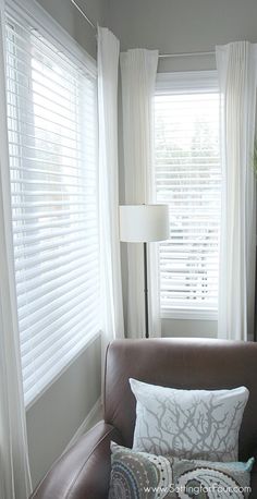 a brown leather chair sitting in front of a window with white drapes on it