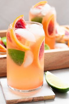 two glasses filled with lemonade and grapefruit on top of a cutting board