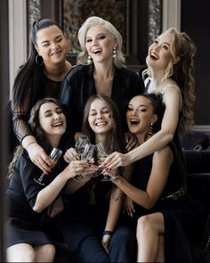 a group of women sitting next to each other holding wine glasses in their hands and laughing