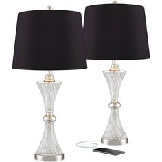 two clear glass lamps with black shades and a remote control next to each other on a white background