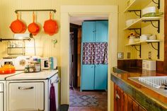 an old fashioned kitchen with orange pots hanging from the ceiling and blue cabinets on the wall