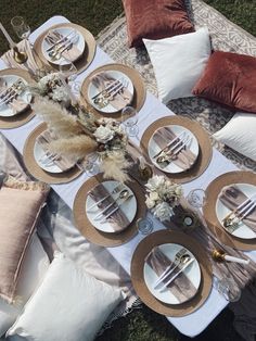 the table is set with plates, silverware and flowers on it for an outdoor dinner