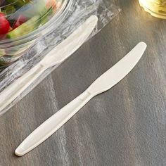 two knives sitting on top of a table next to a bowl of fruit and veggies