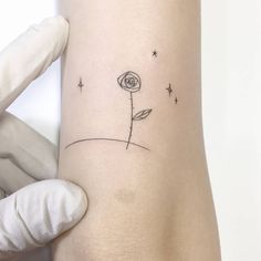 a person with a tattoo on their arm holding up a small flower in front of them