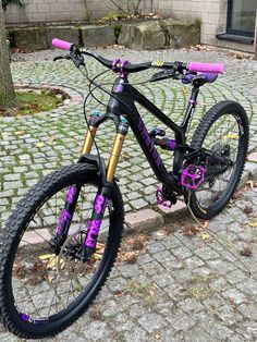 a purple and black bike parked on the side of a brick road next to a tree