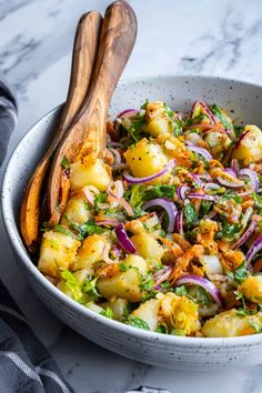 a white bowl filled with potatoes, onions and other vegetables next to a wooden spoon