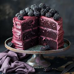 a red velvet cake with blackberries is on a silver platter next to a purple napkin