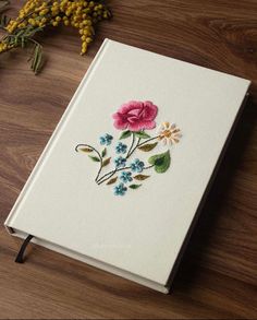 a book with flowers painted on it sitting on a wooden table next to some plants